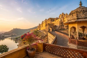 Scenic view of a historic Jaipur fort and palace complex illuminated by golden sunrise light with hills, lake, and traditional Rajasthani architecture.